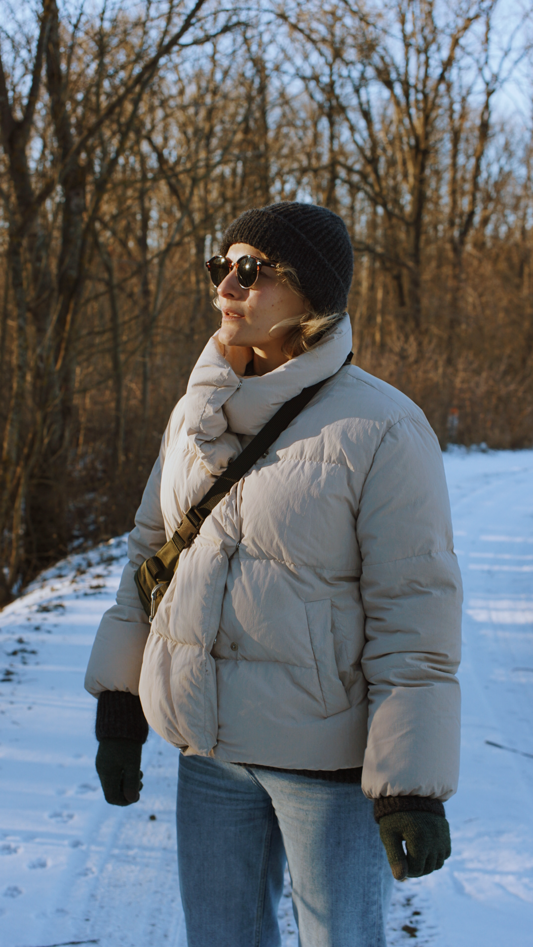 Two people in winter coats embrace in a snowy landscape with bare trees in the background.