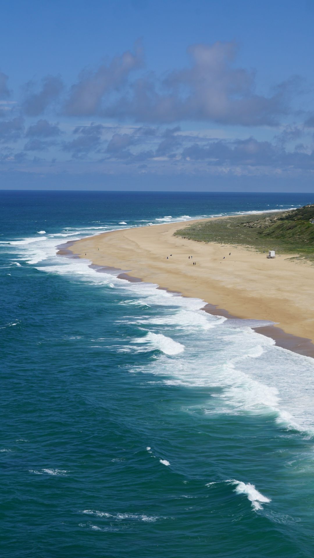 Aerial view of a pristine coastline with turquoise waters meeting golden sandy beach under blue skies.