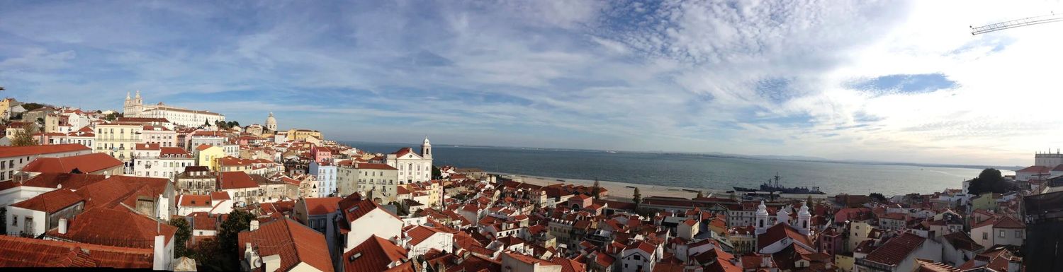 Panoramic cityscape view of Lisbon's coastal buildings and red rooftops.