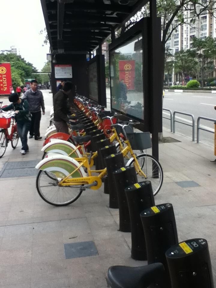 Row of yellow rental bikes parked at a covered station in an urban setting.
