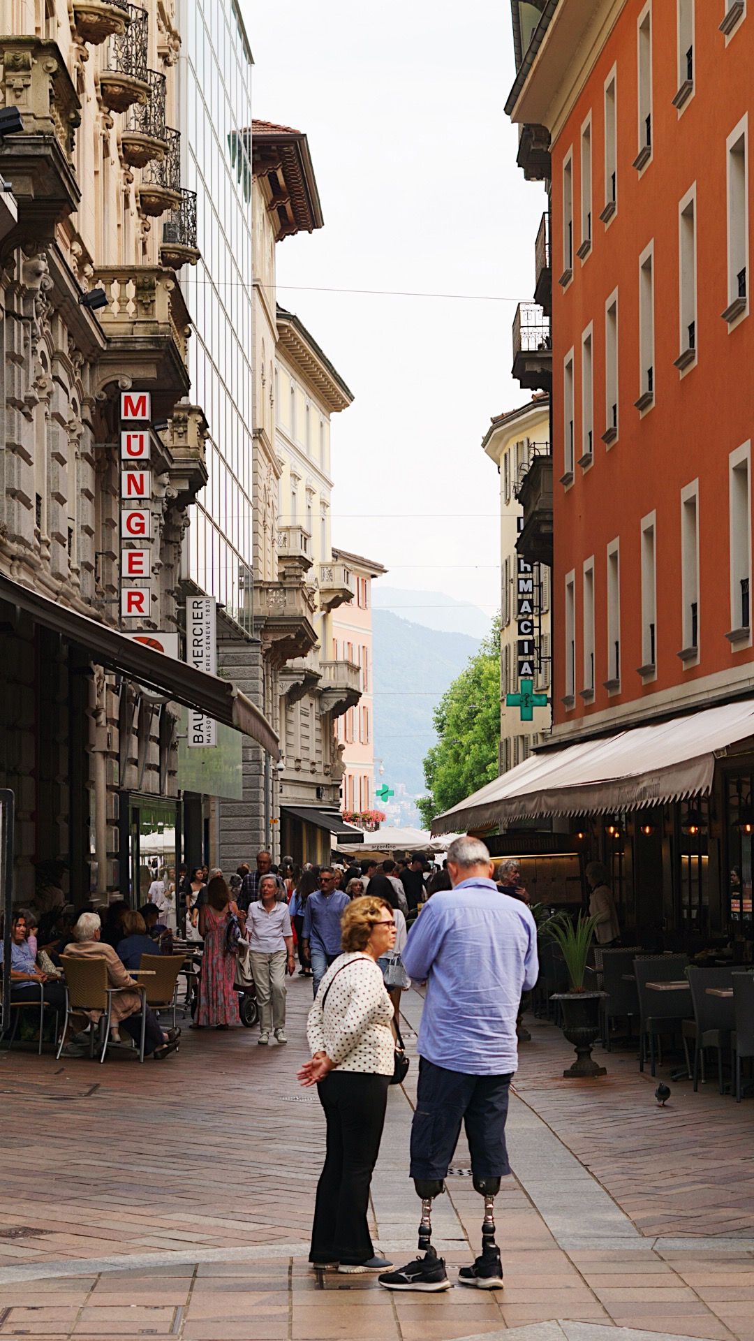 Historic European shopping street with ornate architecture and pedestrians walking.