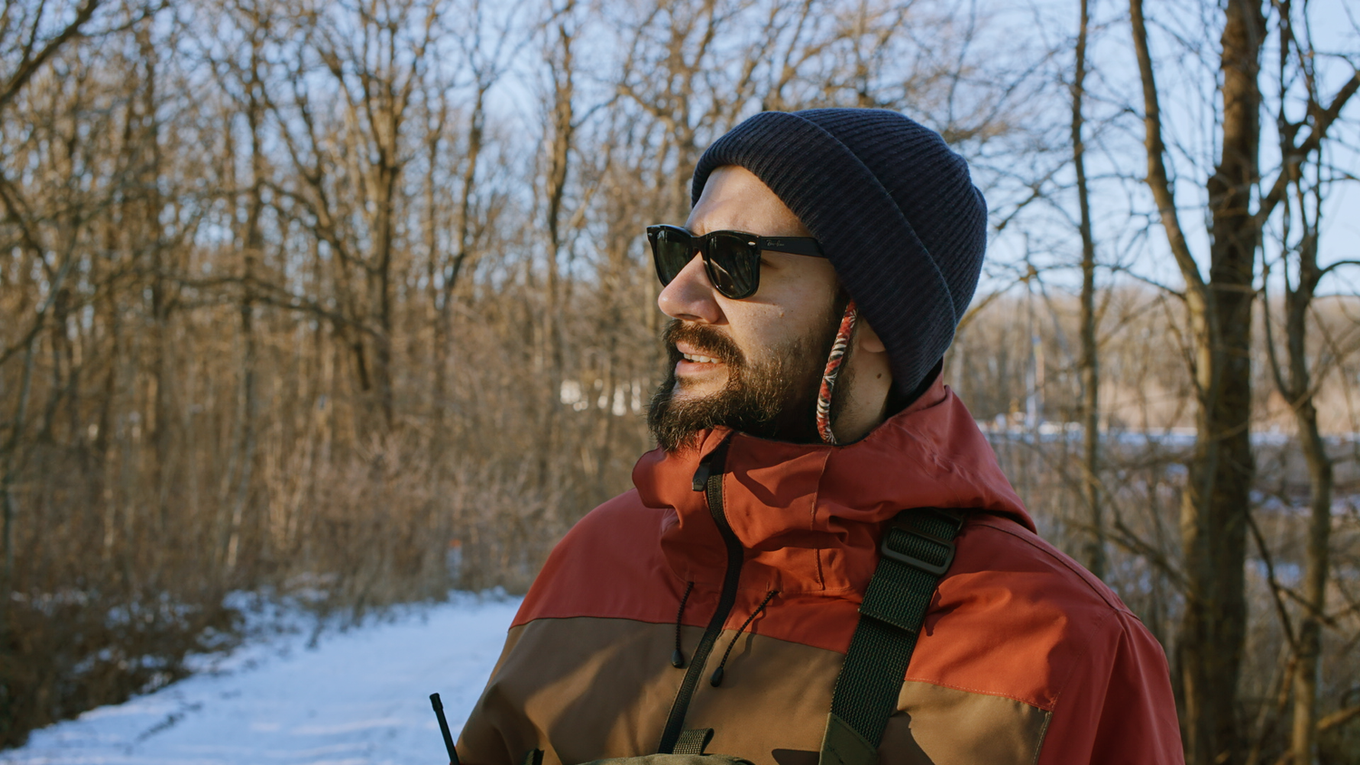A sequence of winter forest scenes showing someone wearing sunglasses and a beanie while walking through snowy woods.