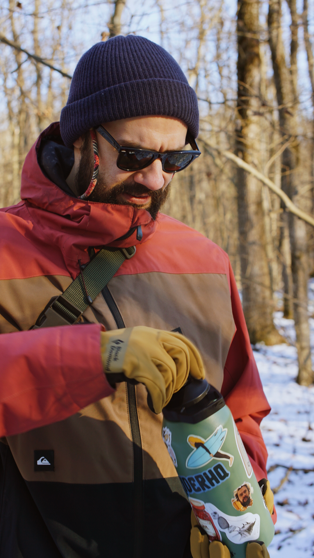 Person in a red and brown winter jacket and navy beanie explores a snow-covered forest trail.