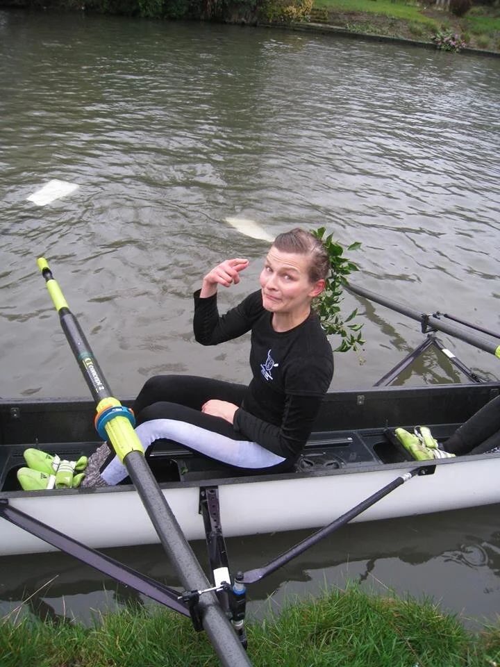 Rowing equipment and oars laid out along a grassy riverbank.
