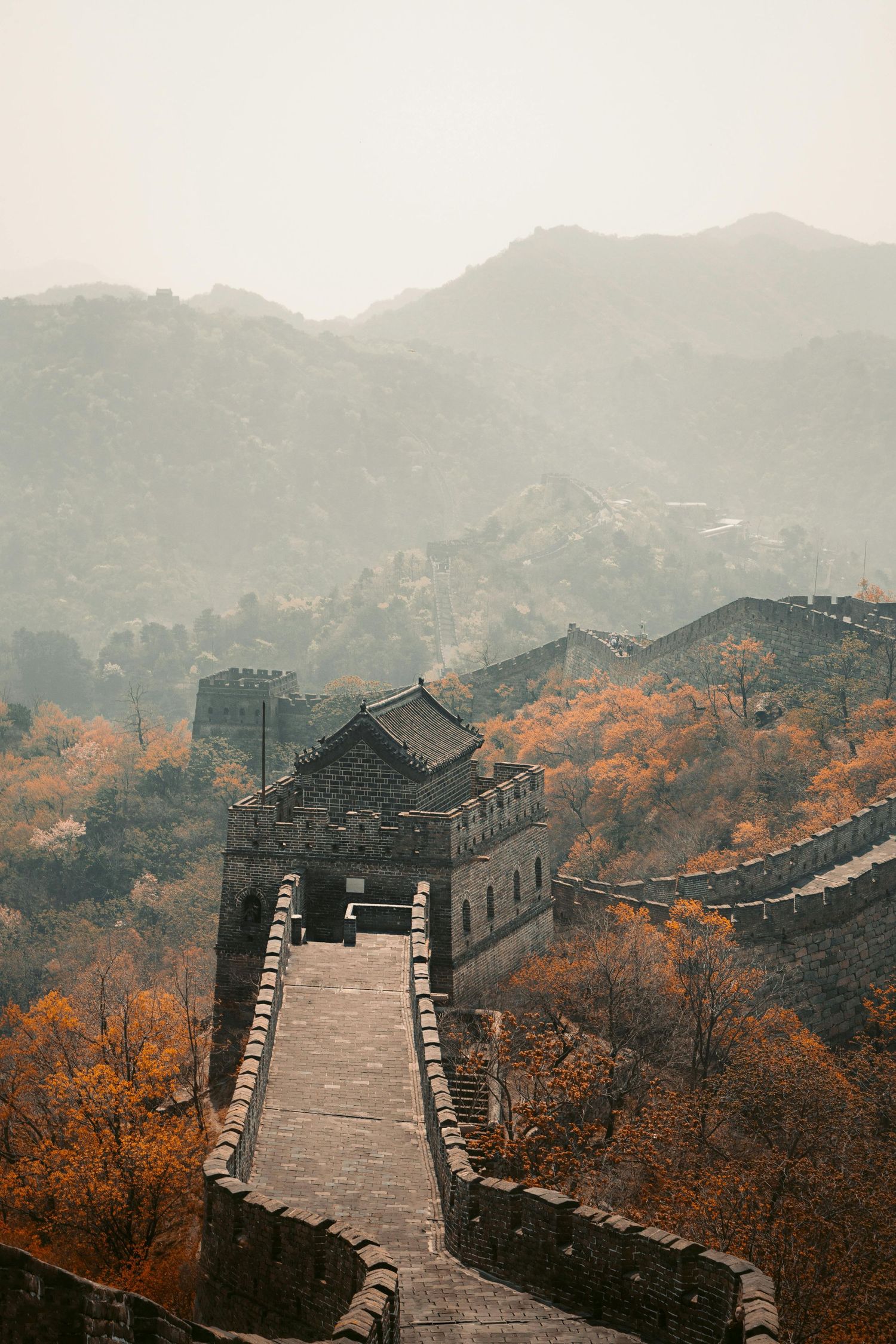 Autumn view of the Great Wall of China winding through misty mountains with orange foliage.