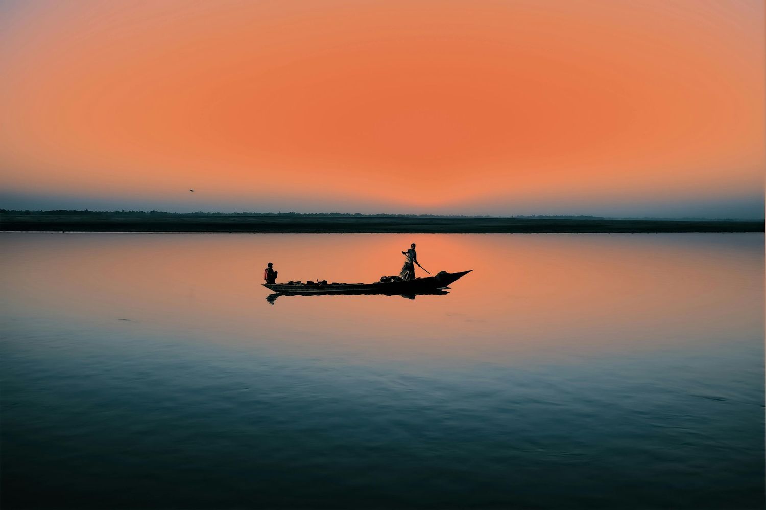 Silhouettes of boats against an orange sunset over calm waters.