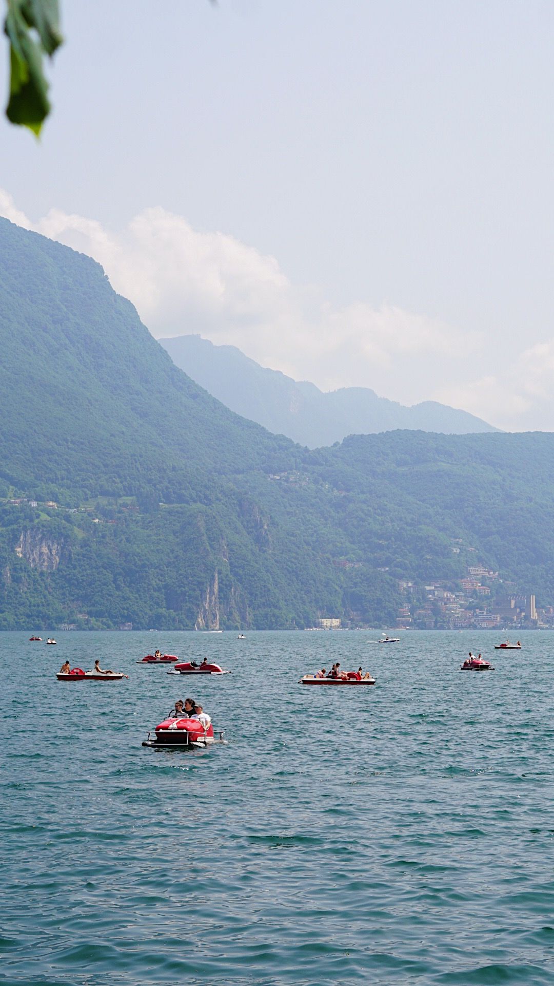 Red speedboats scattered across blue lake waters with mountain landscape in background.