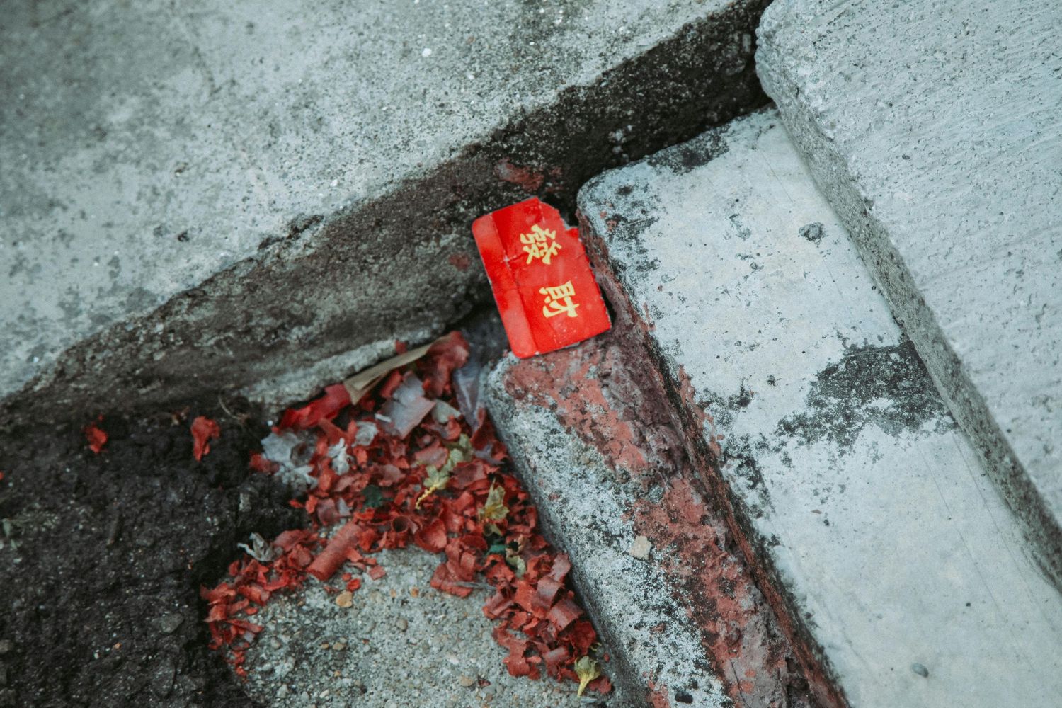 Red firecracker debris scattered on grey concrete ground after celebration.