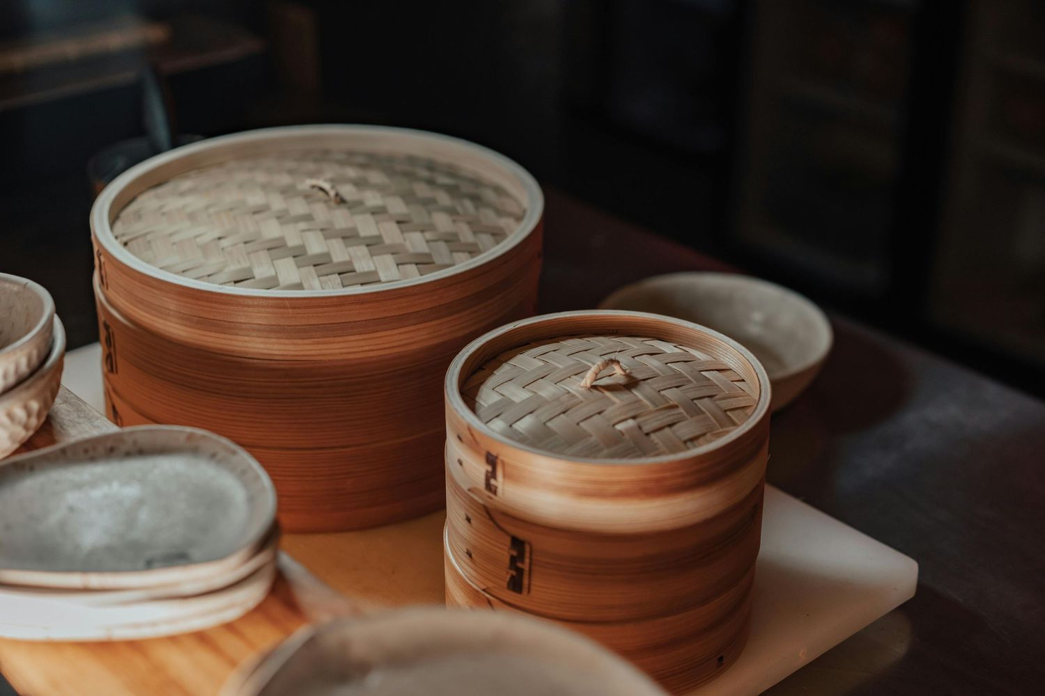 Bamboo steamer baskets stacked on wooden surface in dim lighting.