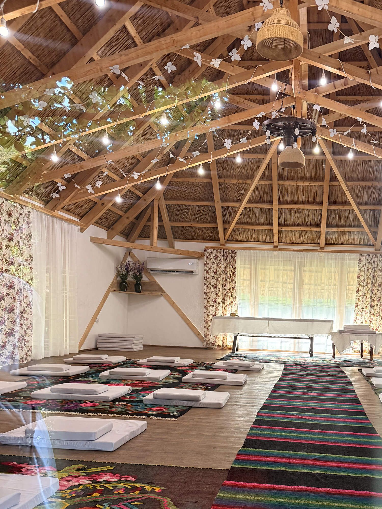 Rustic open-air yoga studio with thatched roof, string lights, colorful mats, and bohemian decor for retreat sessions.