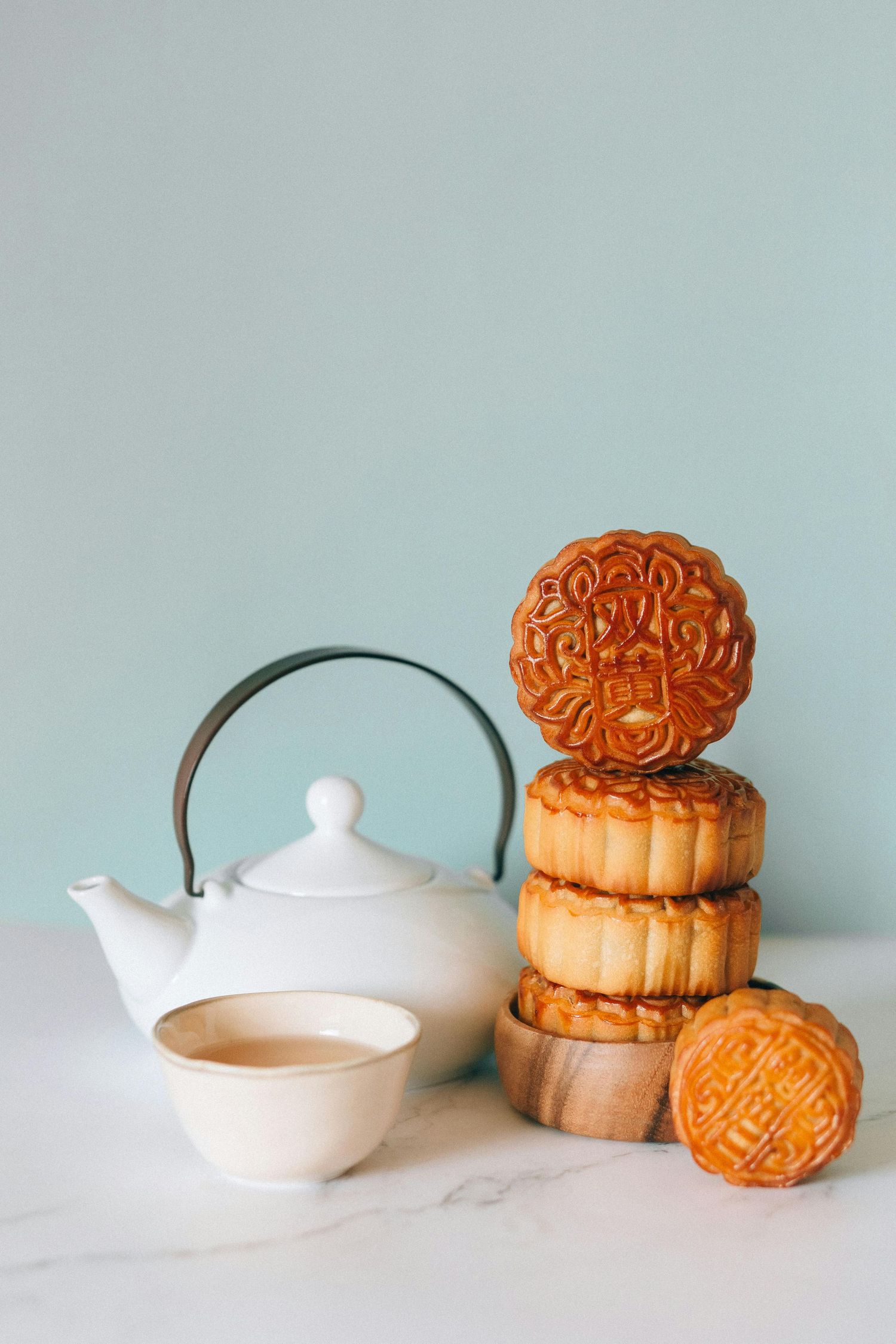 Traditional mooncakes arranged with white ceramic teapot on minimal background.
