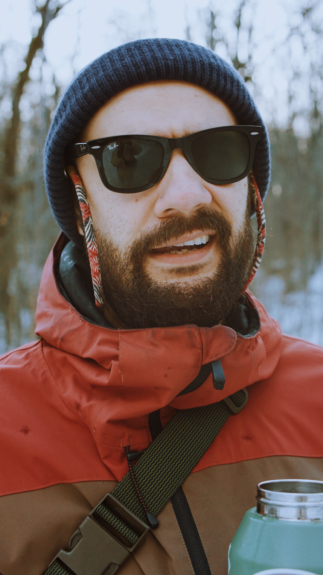 A close-up series of someone wearing sunglasses, a beanie hat and orange winter jacket while holding a beverage can.