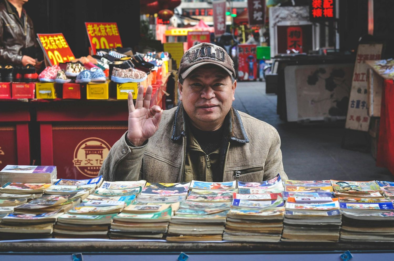 Street market stall displaying rows of books with colorful covers and signs.