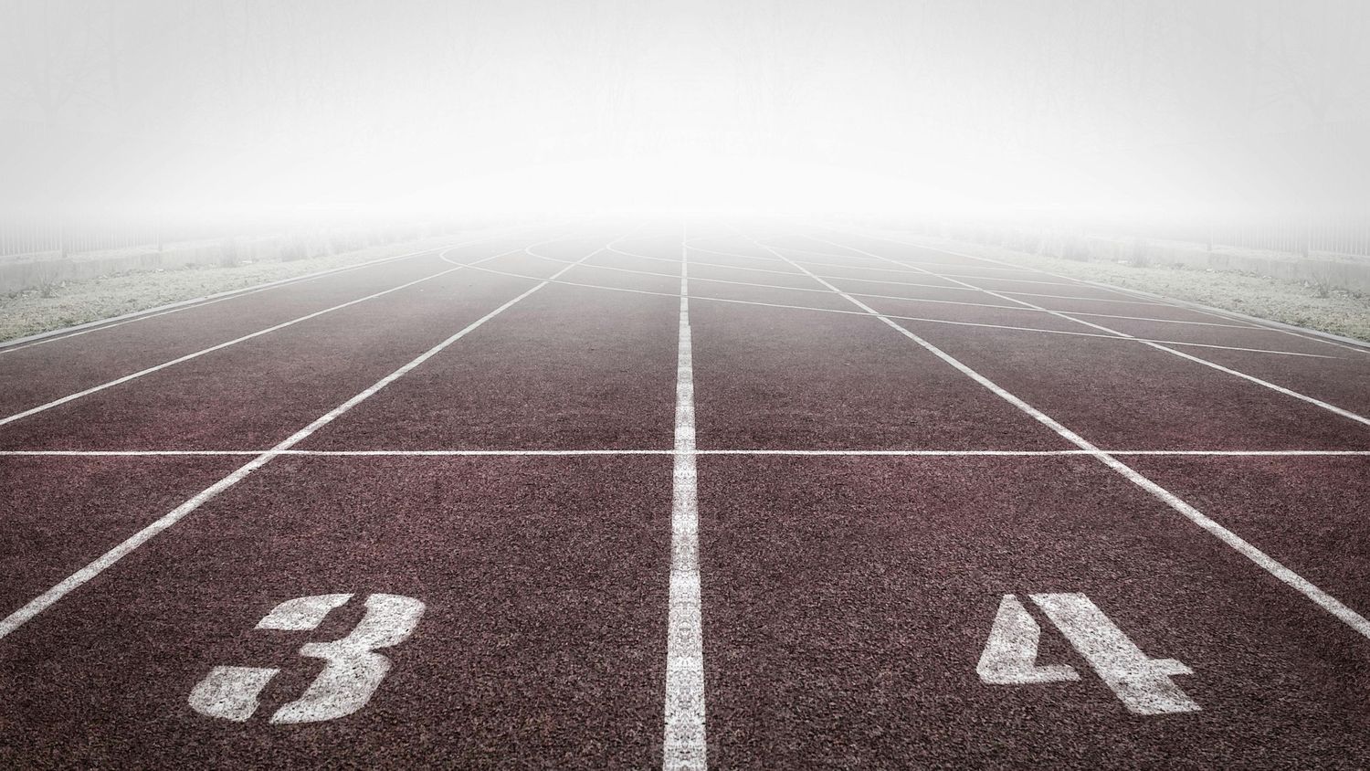 Running track lanes marked with numbers on red surface stretching into foggy distance.