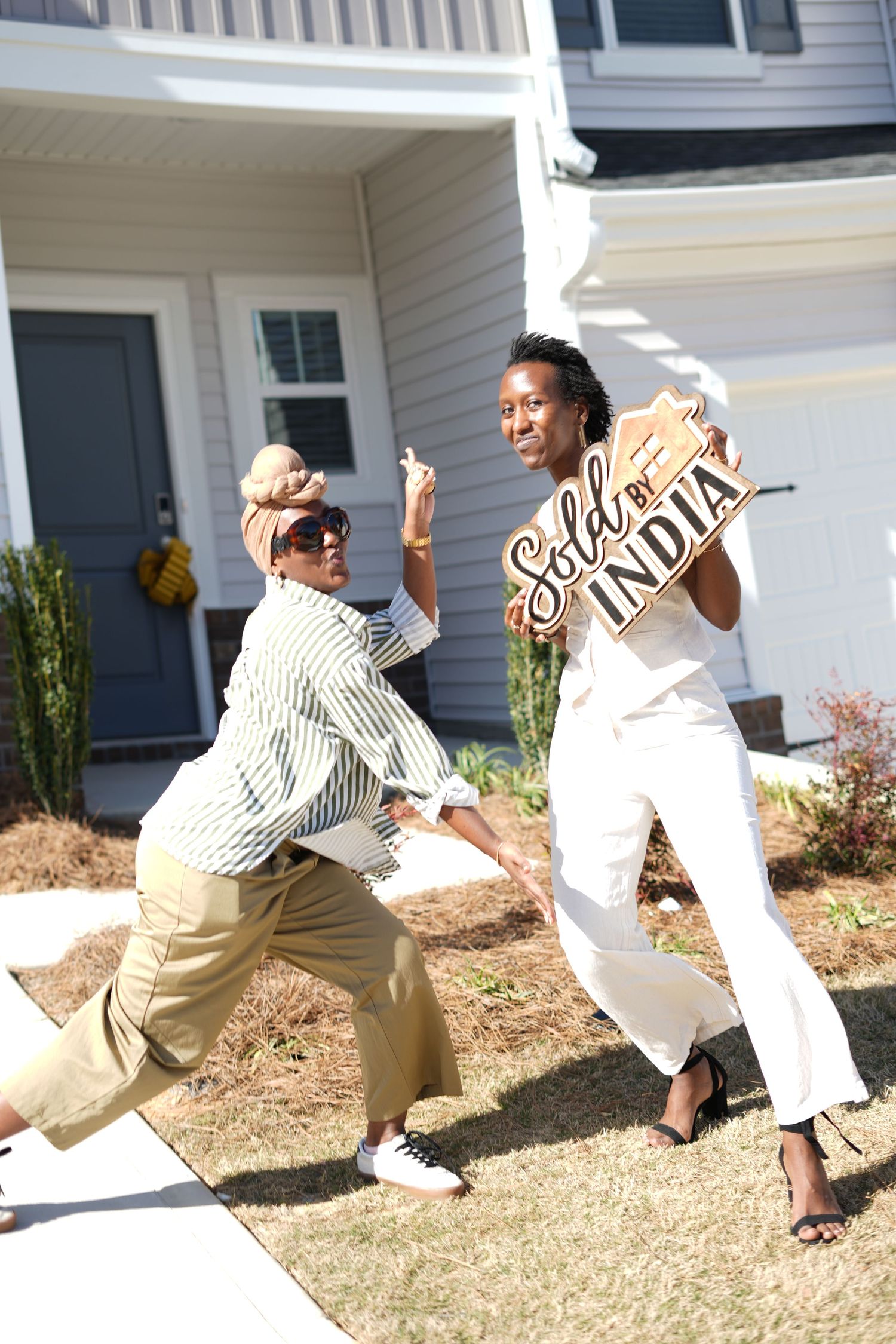 Two people in casual attire striking playful poses outside a white house.