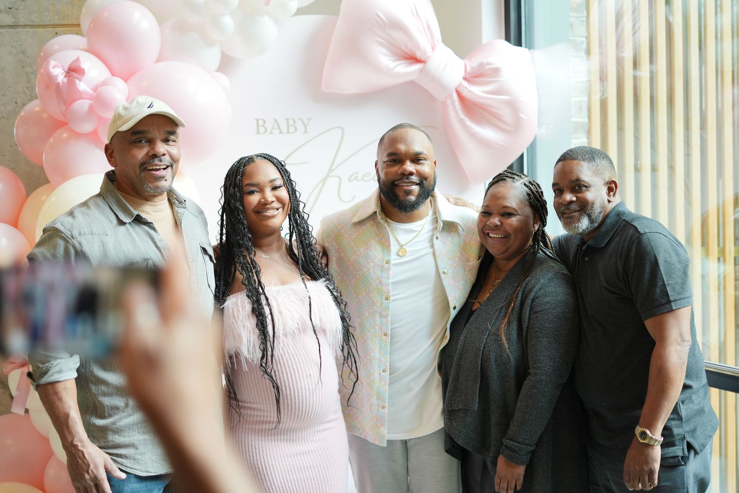 Group photo at baby shower celebration with pink balloon decorations and festive atmosphere.