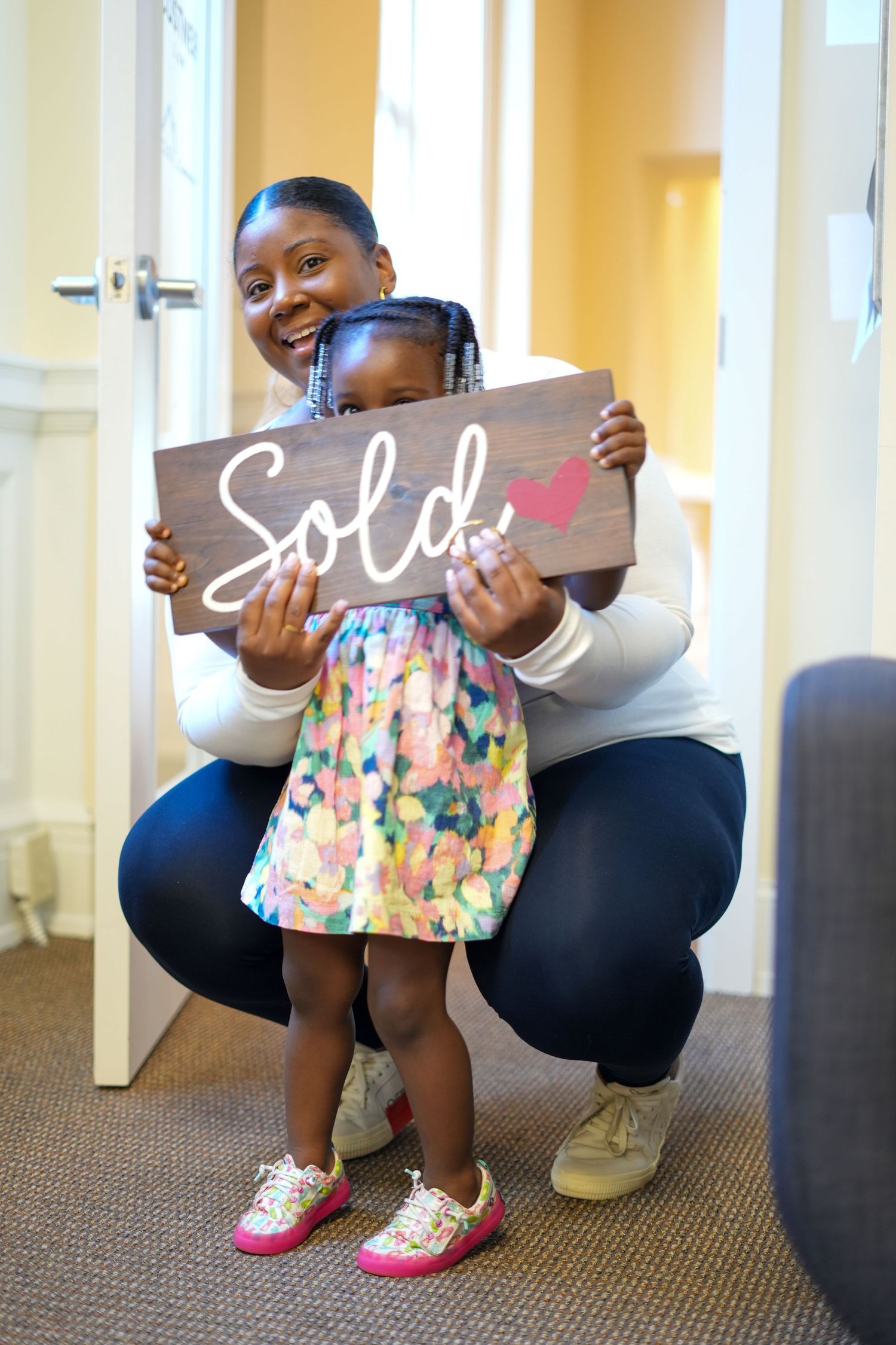 Adult and child holding 'Sold' sign indoors.