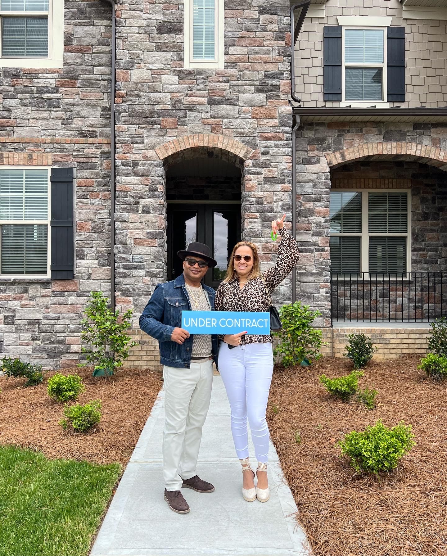 Two people holding a welcome sign in front of a stone facade townhouse.