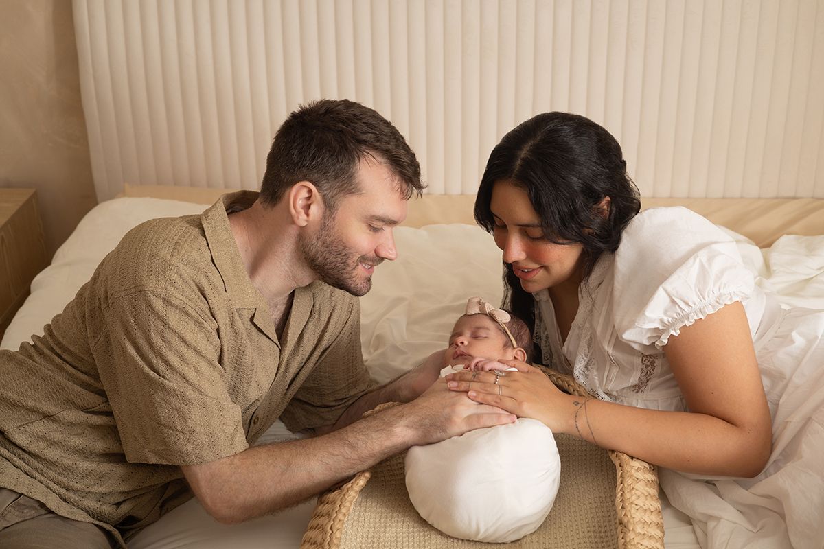 Parents tenderly gazing at their newborn baby during a professional newborn photography session on a bed.