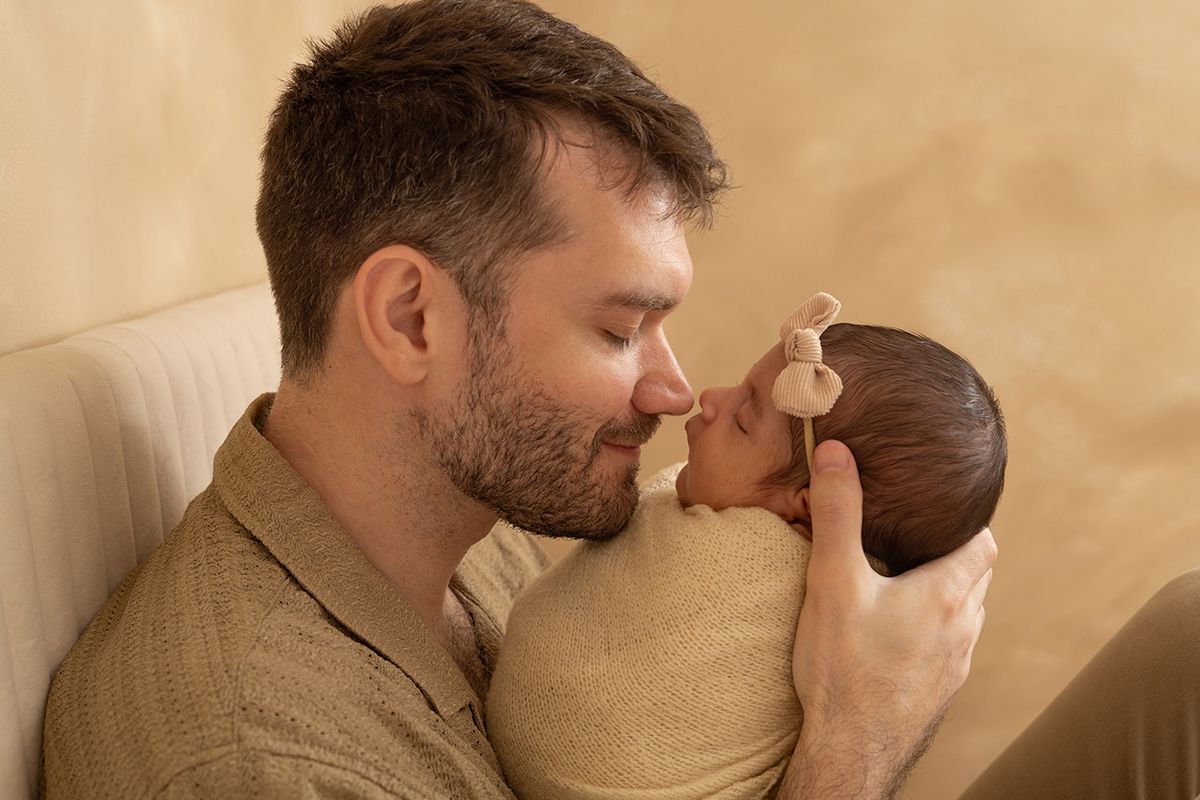 A father tenderly touches noses with his newborn baby, cradling the infant gently in a warm, softly lit setting.