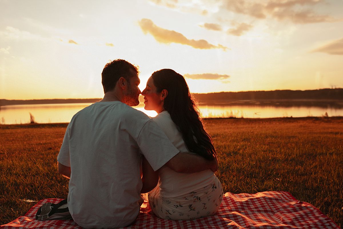 Romantic couple sharing a kiss at sunset while sitting on a picnic blanket by a lake near Atlanta, Georgia.