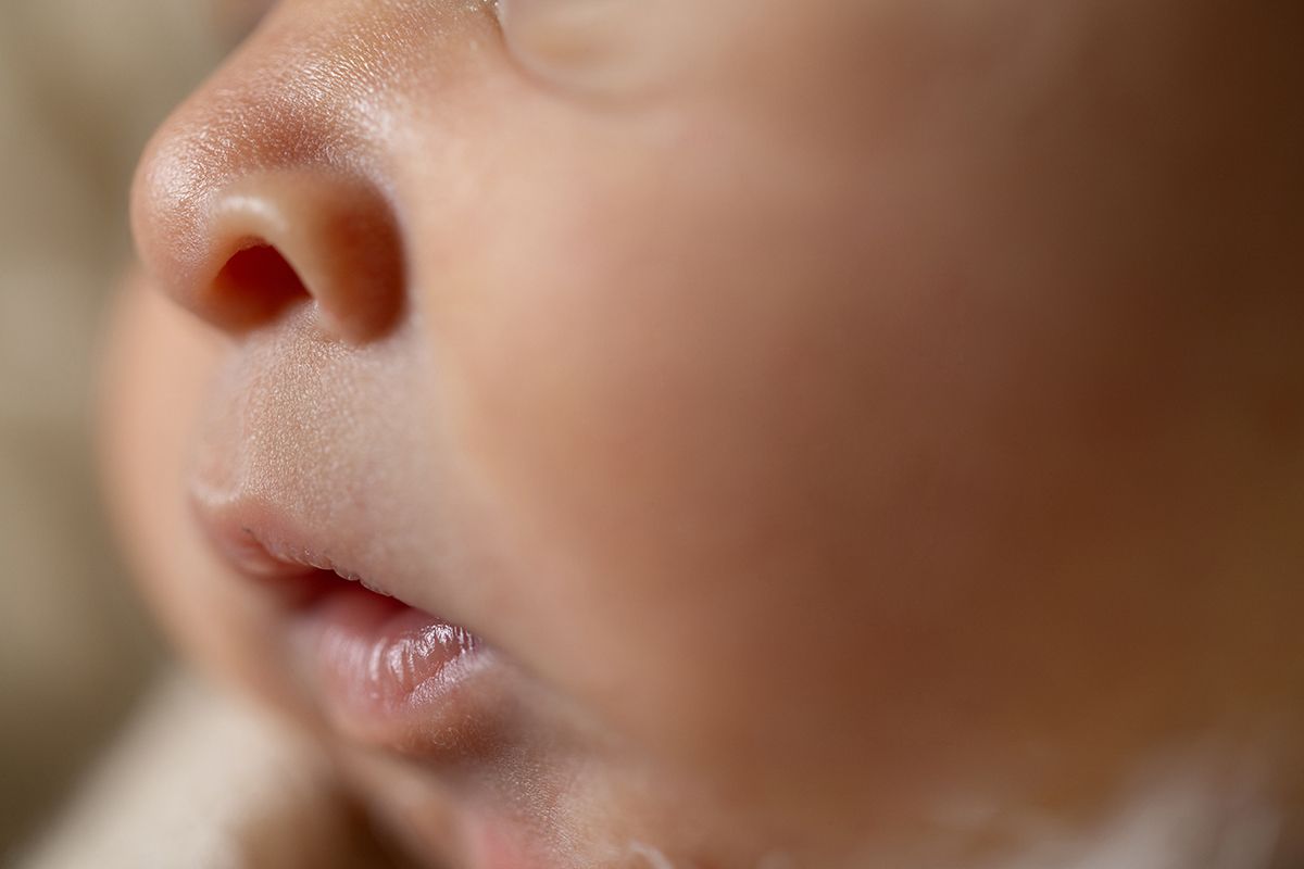 Close-up macro photo of a newborn baby's nose, lips, and soft skin with a blurred warm background.