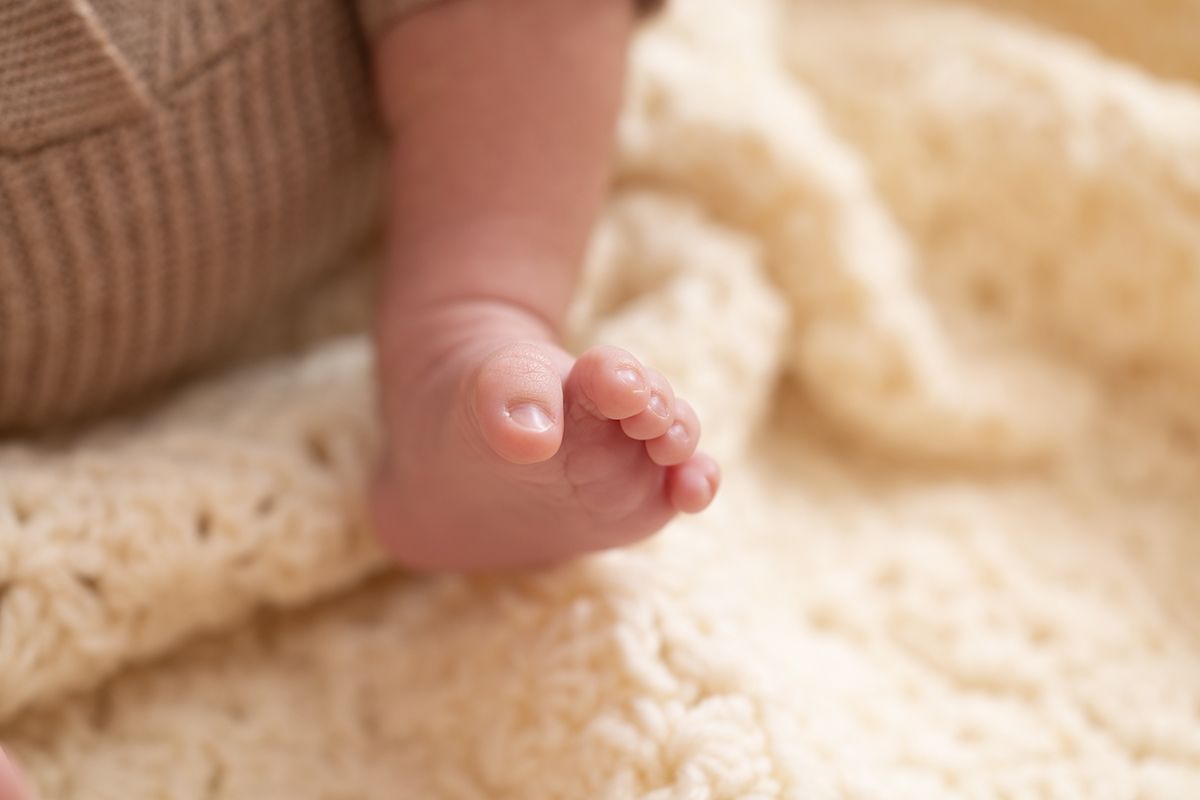 Close-up of a newborn baby's tiny feet resting on a soft cream knit blanket.