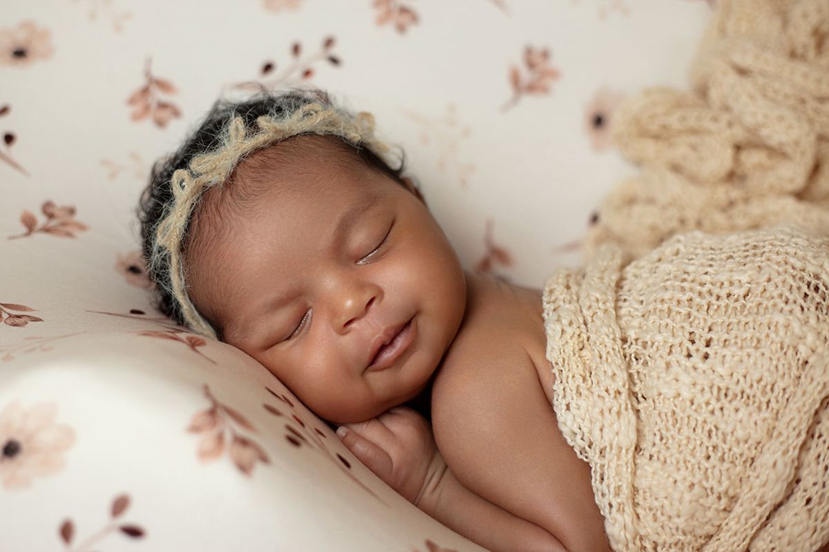 Peaceful newborn baby sleeping wrapped in cream knit blanket wearing floral bonnet on soft floral background.