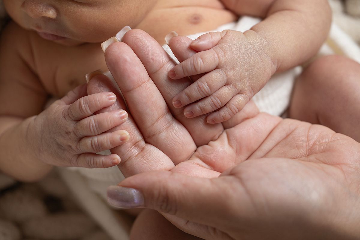 Close-up of a newborn baby's tiny hands and feet resting gently in an adult's open palm.