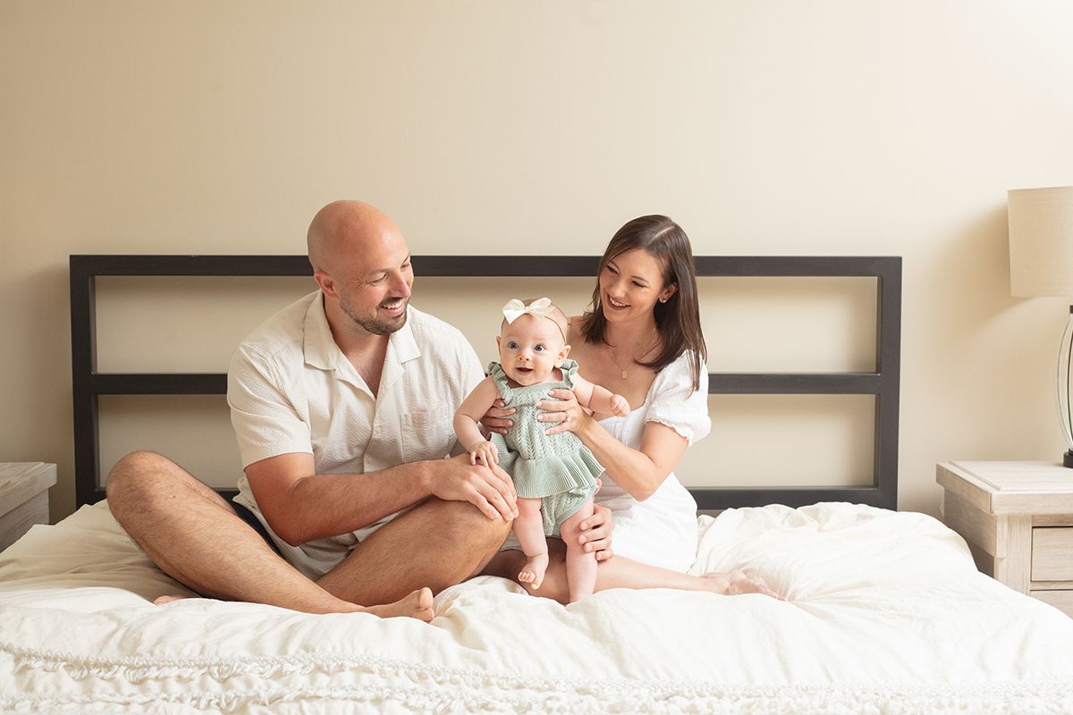 Natural family portrait of mother, father, and baby in a cozy bedroom setting
