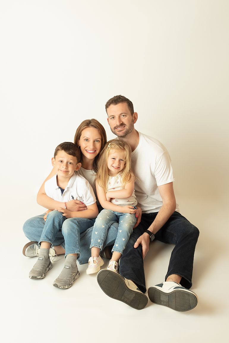 Happy family of four sitting together smiling, parents with boy and girl in jeans, white studio background.