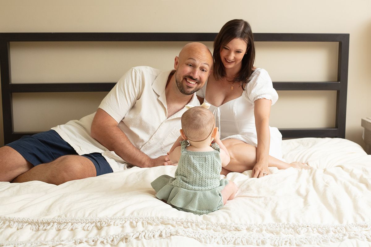 In-home lifestyle family session with parents and baby sitting on a bed in Douglasville, Georgia