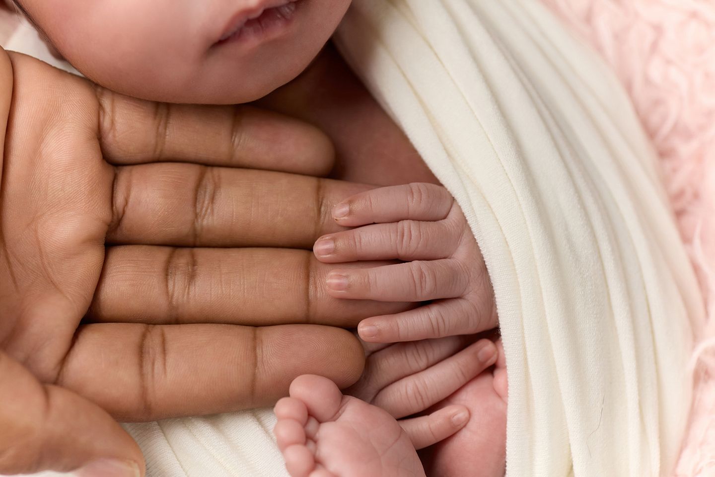 Close-up of a newborn baby's tiny hands resting on an adult's large hand, wrapped in a soft white blanket.