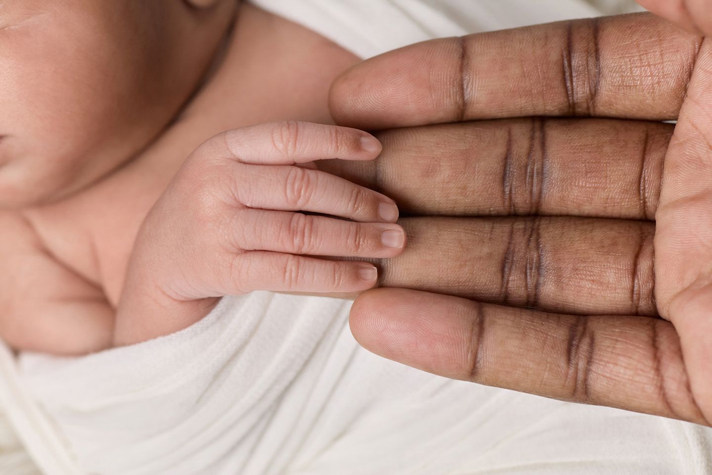 Newborn baby's tiny hand resting in the palm of an adult's large dark-skinned hand.