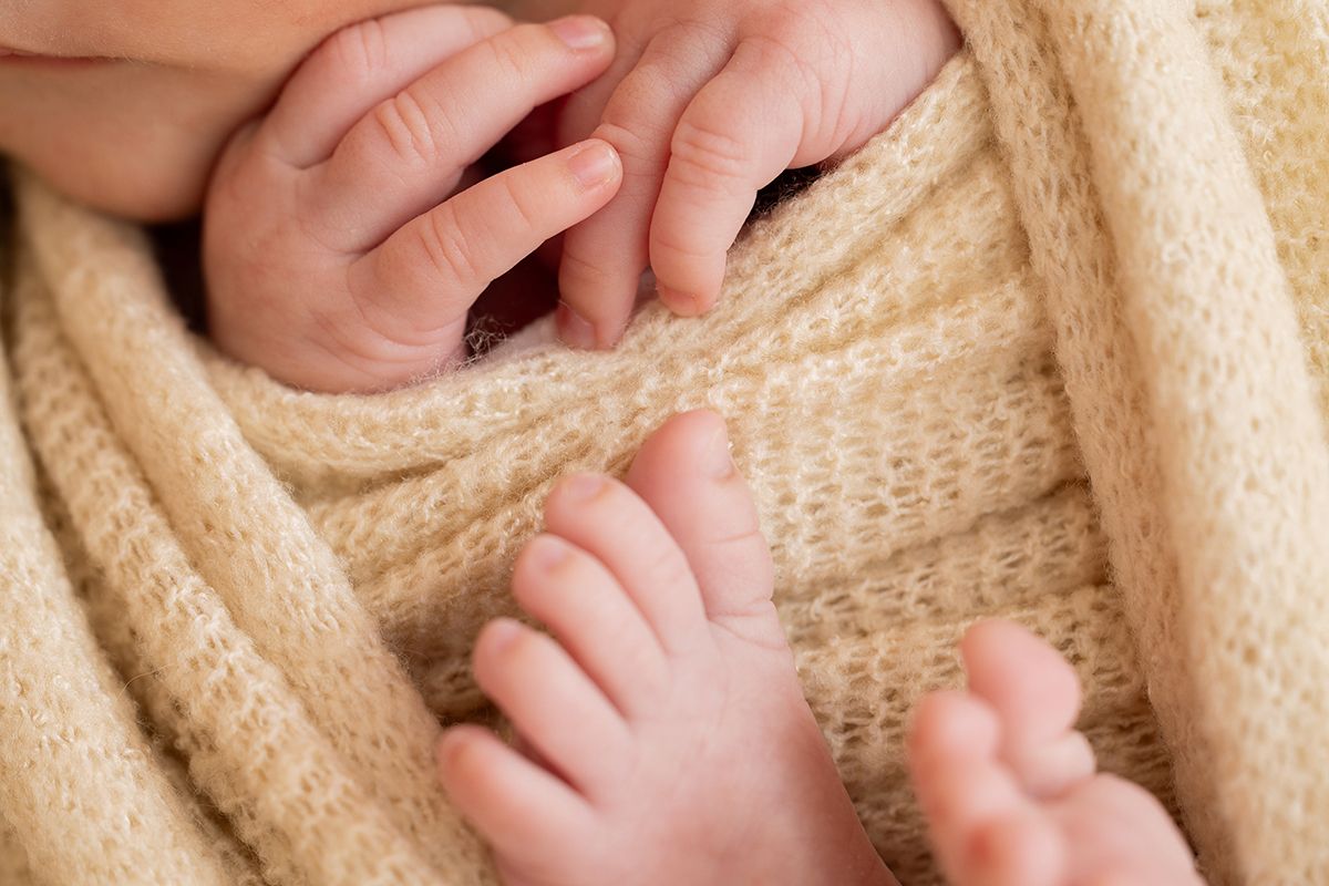 Close-up of newborn baby tiny feet and toes wrapped in soft beige knit blanket.