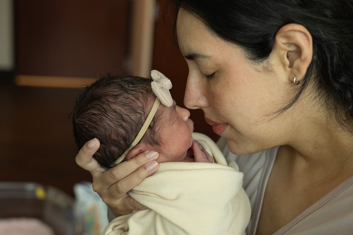 A mother tenderly kisses her newborn baby wrapped in a white blanket, sharing a precious bonding moment.