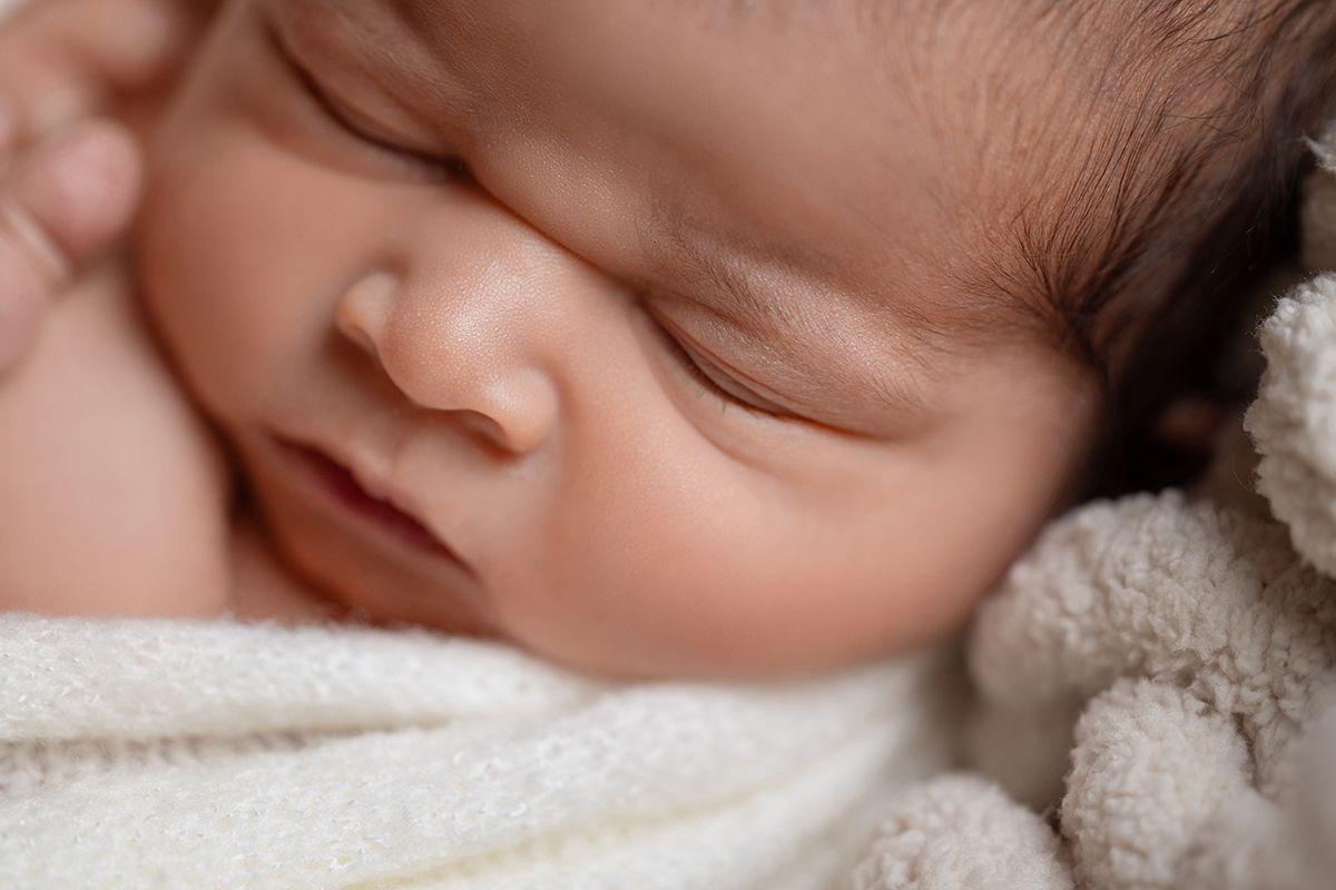 Close-up of a peaceful sleeping newborn baby wrapped in a soft white blanket with a teddy bear nearby.
