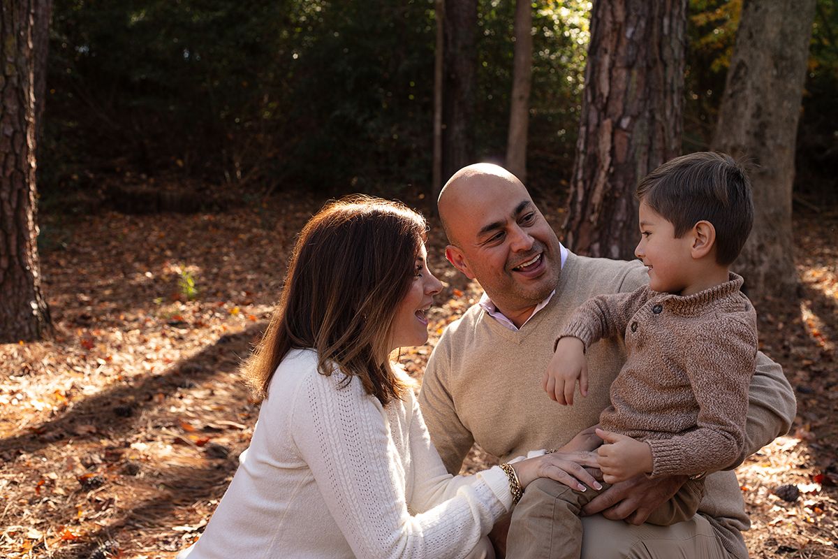 Family of three sharing a joyful moment outdoors in a sunlit forest, parents smiling at toddler son.
