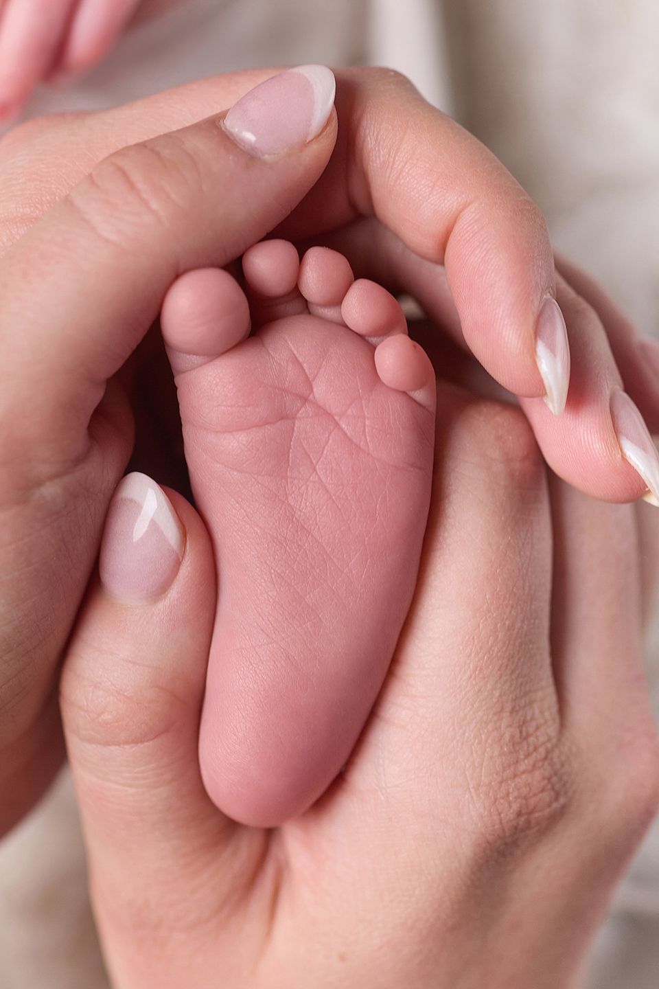 Close-up of a newborn baby's tiny foot cradled gently in mother's hands with French manicured nails.