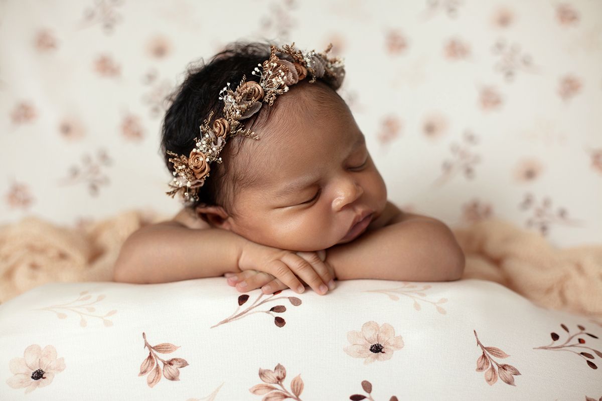 Newborn baby girl sleeping peacefully wearing a floral headband on a soft floral blanket.