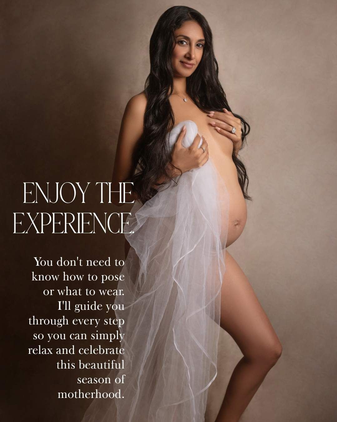 Expecting mother draped in white tulle fabric poses elegantly for professional maternity photos.