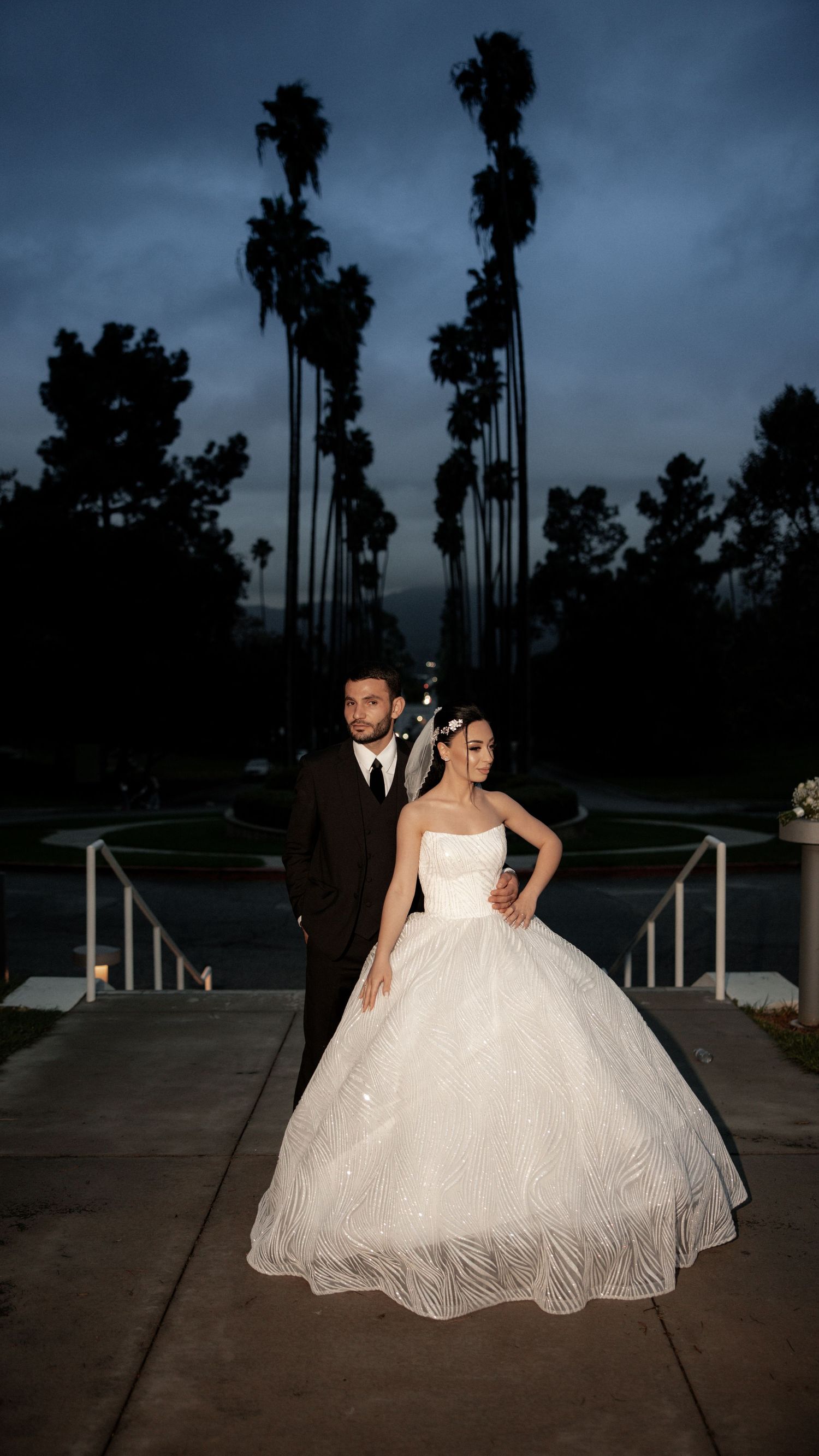 Romantic evening wedding photo with palm trees silhouetted against a dusky sky.