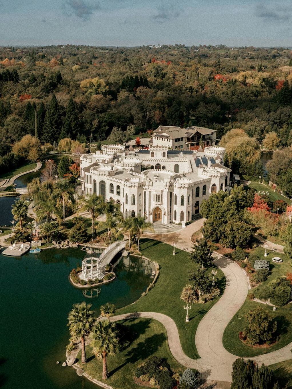 Aerial view of stunning white castle wedding venue surrounded by lush gardens and scenic lake.