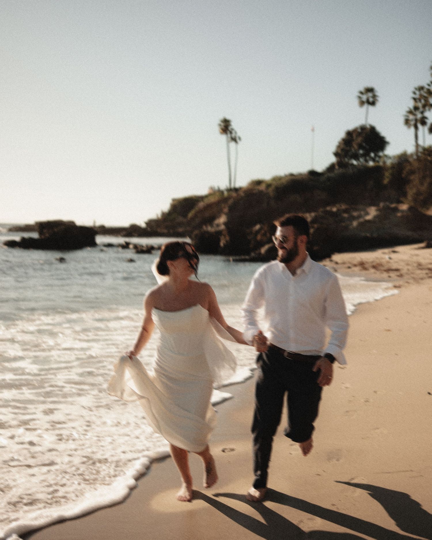 A couple walks hand in hand along a beach shoreline during sunset.