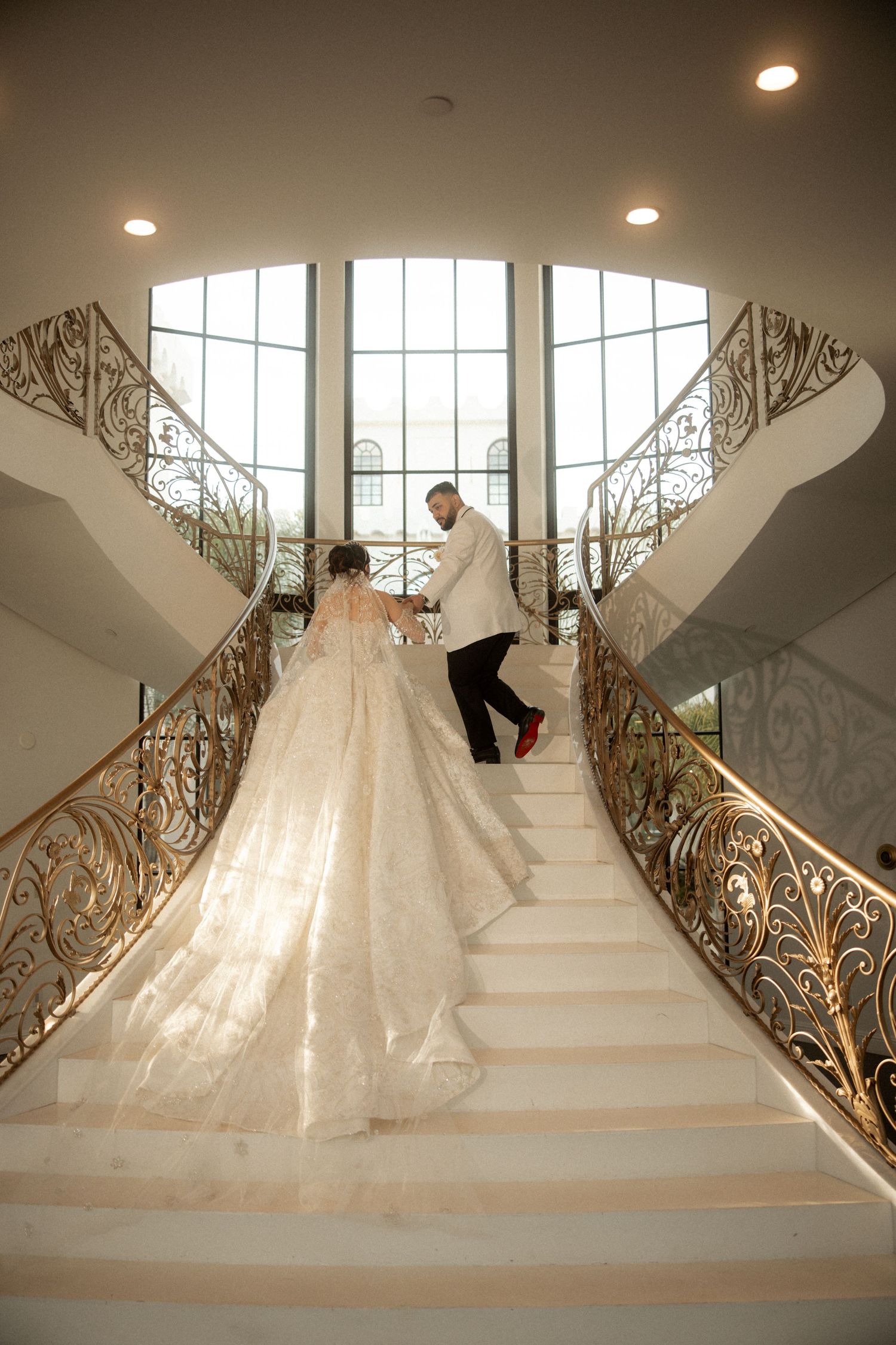 Bride and groom ascending grand staircase with ornate gold railings in elegant wedding venue.