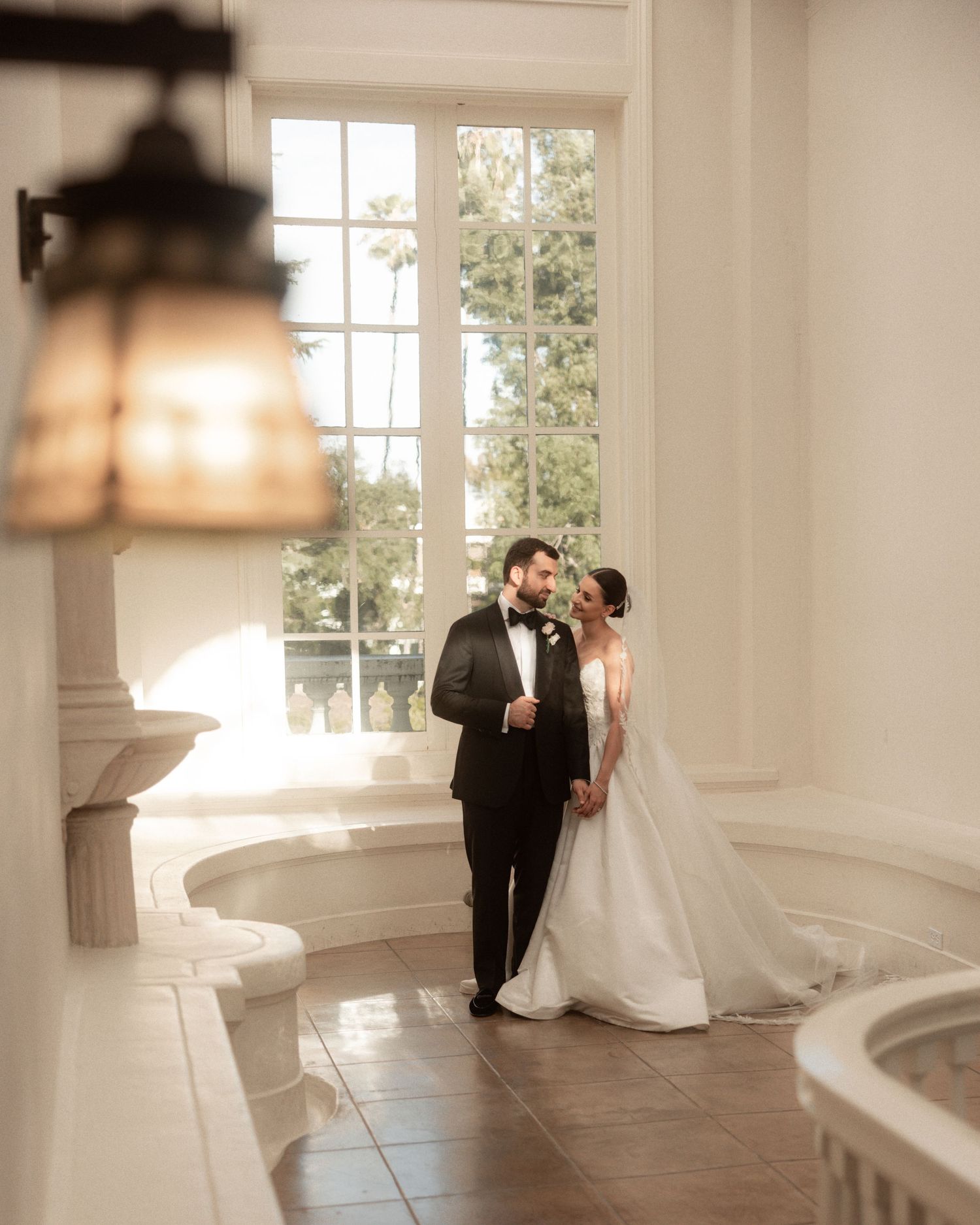 Bride and groom sharing an intimate moment in a sunlit elegant venue interior.