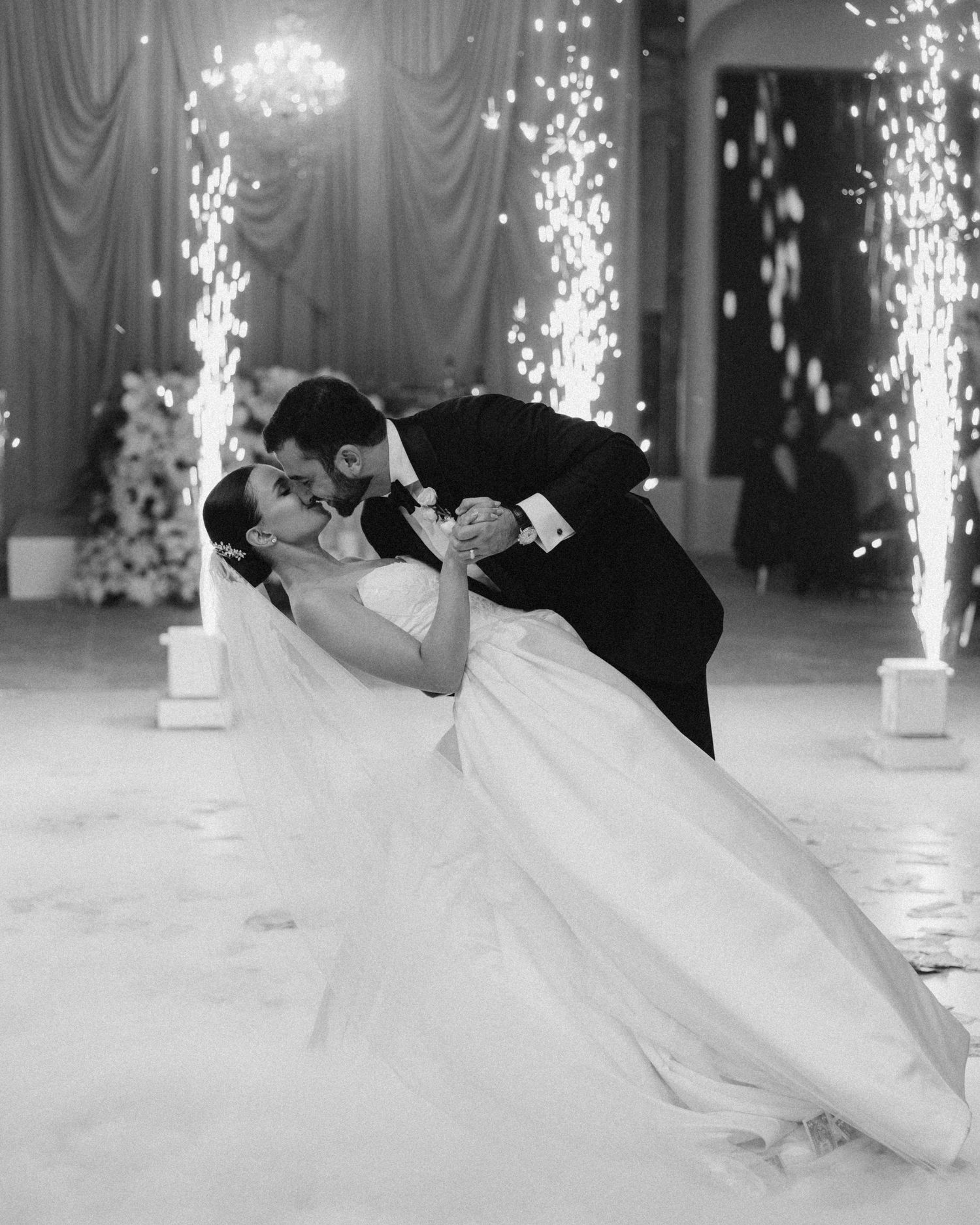 Black and white photo of bride and groom sharing a dip kiss on the dance floor with sparklers.