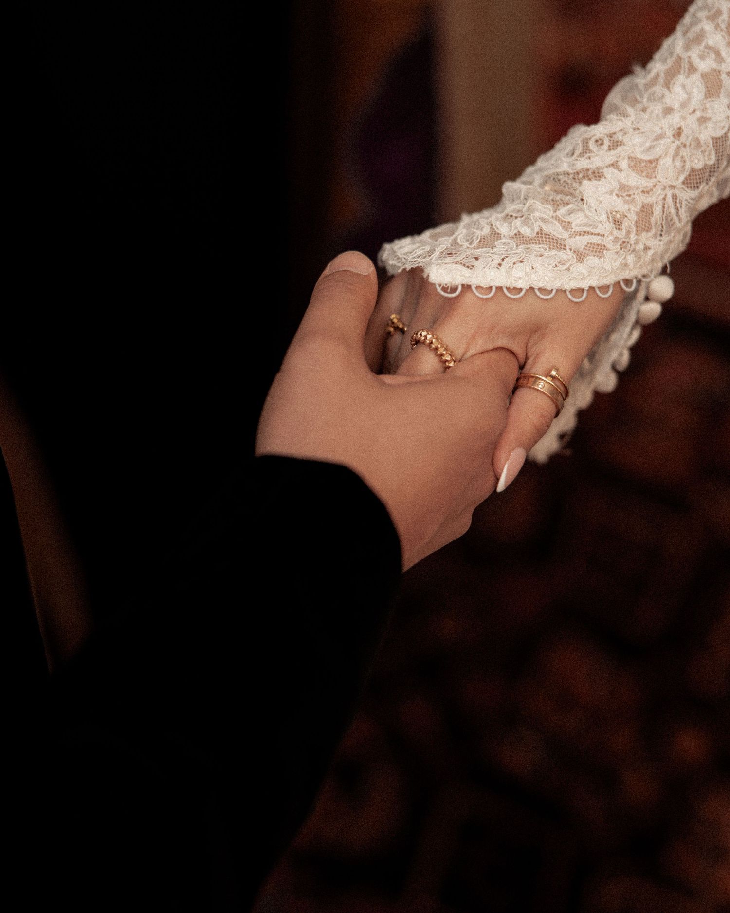 Close-up of hands wearing wedding rings against lace fabric in warm lighting.