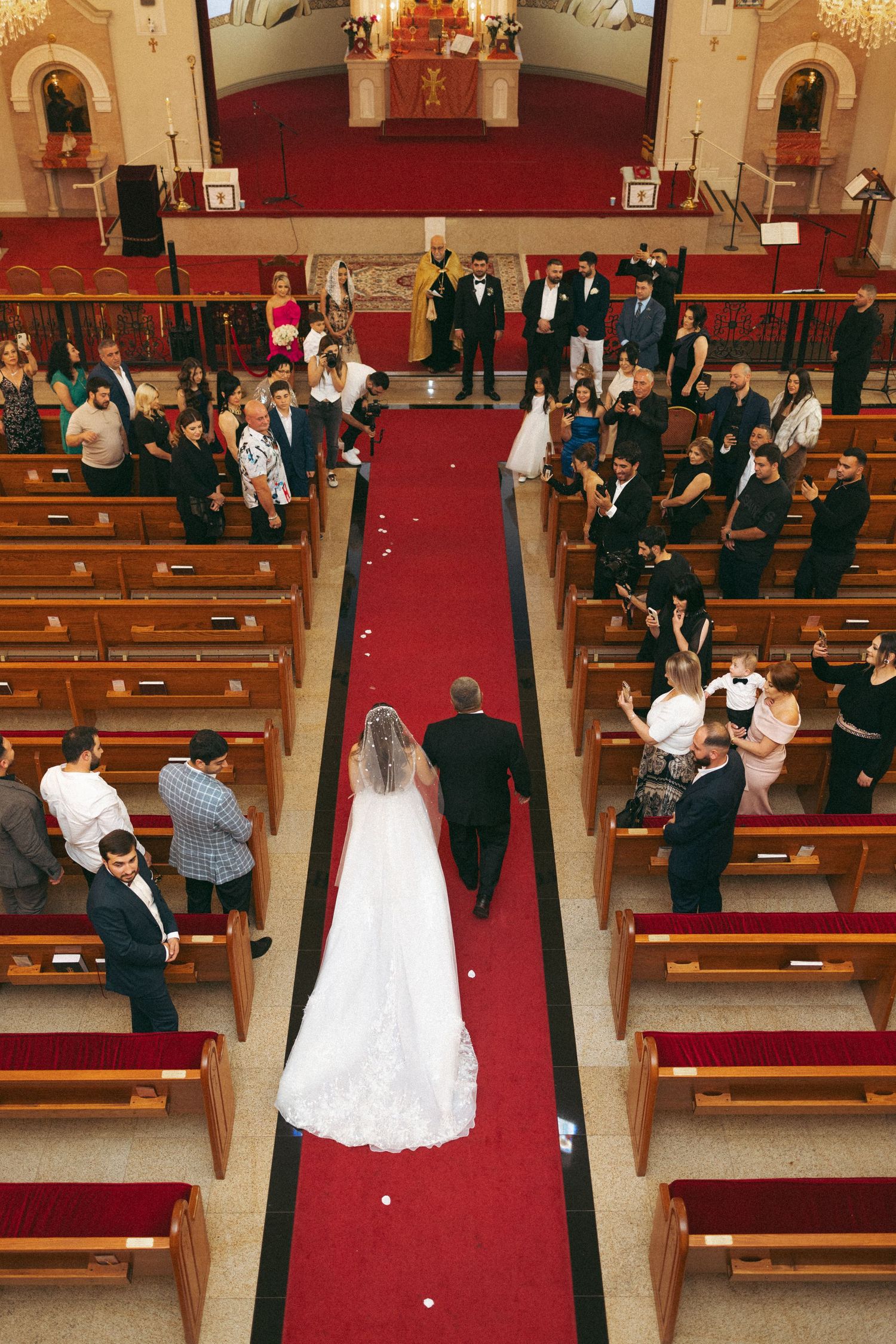 Aerial view of a bride walking down a red-carpeted church aisle with wedding guests.