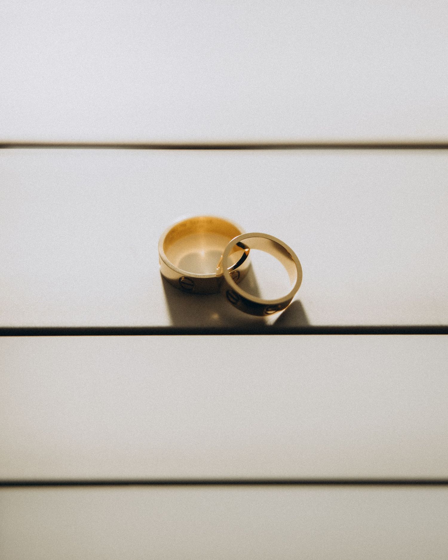 Two gold wedding bands resting together on a white striped surface.